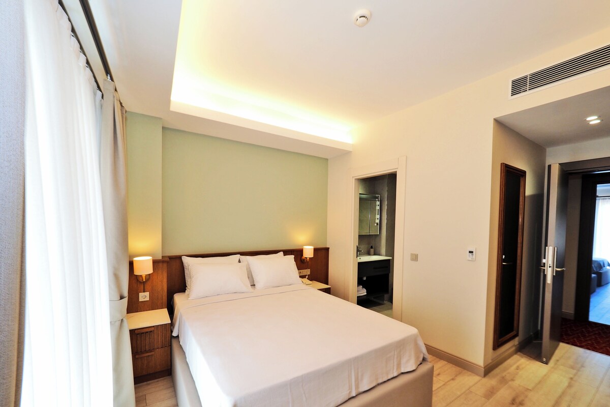 Une chambre d’hôtel comprenant un lit, des lampes de chevet, une table de chevet, un miroir et une porte donnant sur une autre pièce.
