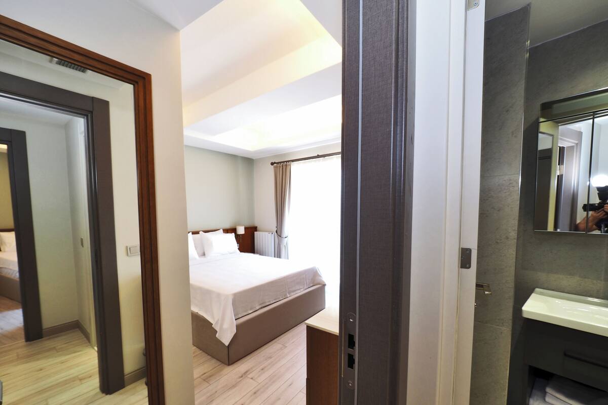 A hotel room with a bed, a bathroom with a mirror, and a view of the outside.