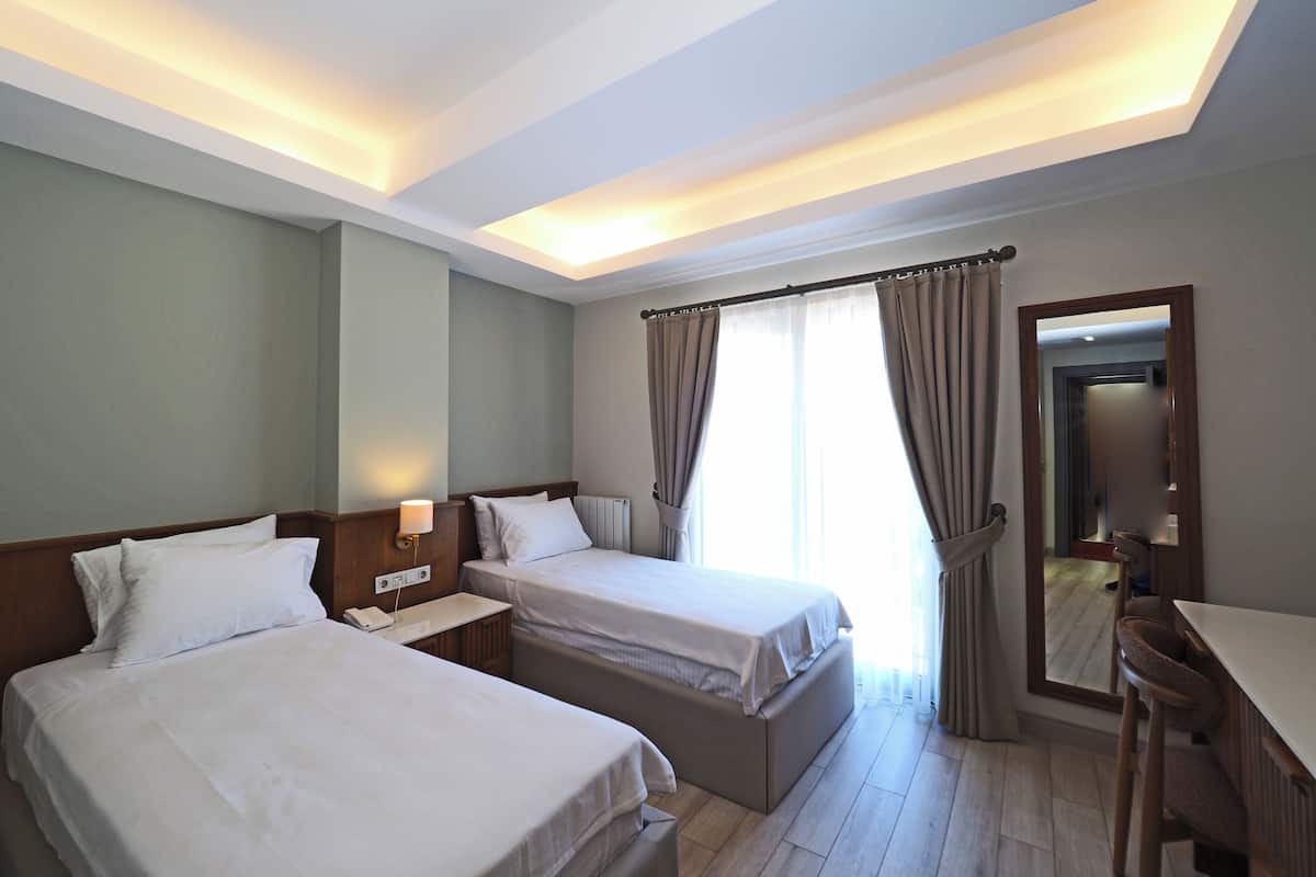 A hotel room with two beds, a desk, a chair, a mirror, and a window with curtains.