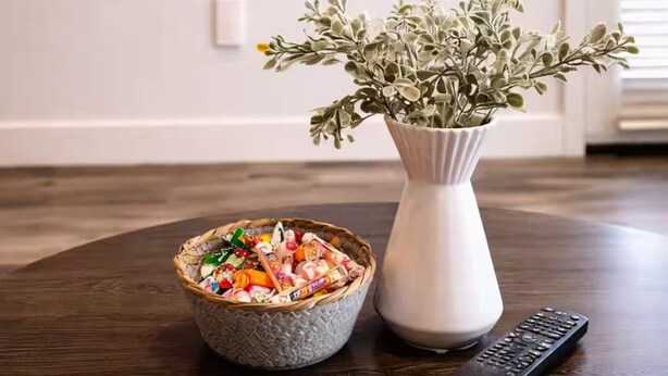 Ein Esstisch mit einer Schüssel verschiedener Snacks, einer Vase mit Grünpflanzen und einer Fernbedienung.