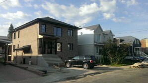 Una casa de maó de dos pisos amb un porxo davanter, una furgoneta SUV negra aparcada al davant i un cel serè.