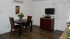 Zona de menjador amb taula, cadires, un ram de flors, aire condicionat, televisió sobre un suport i una porta.
