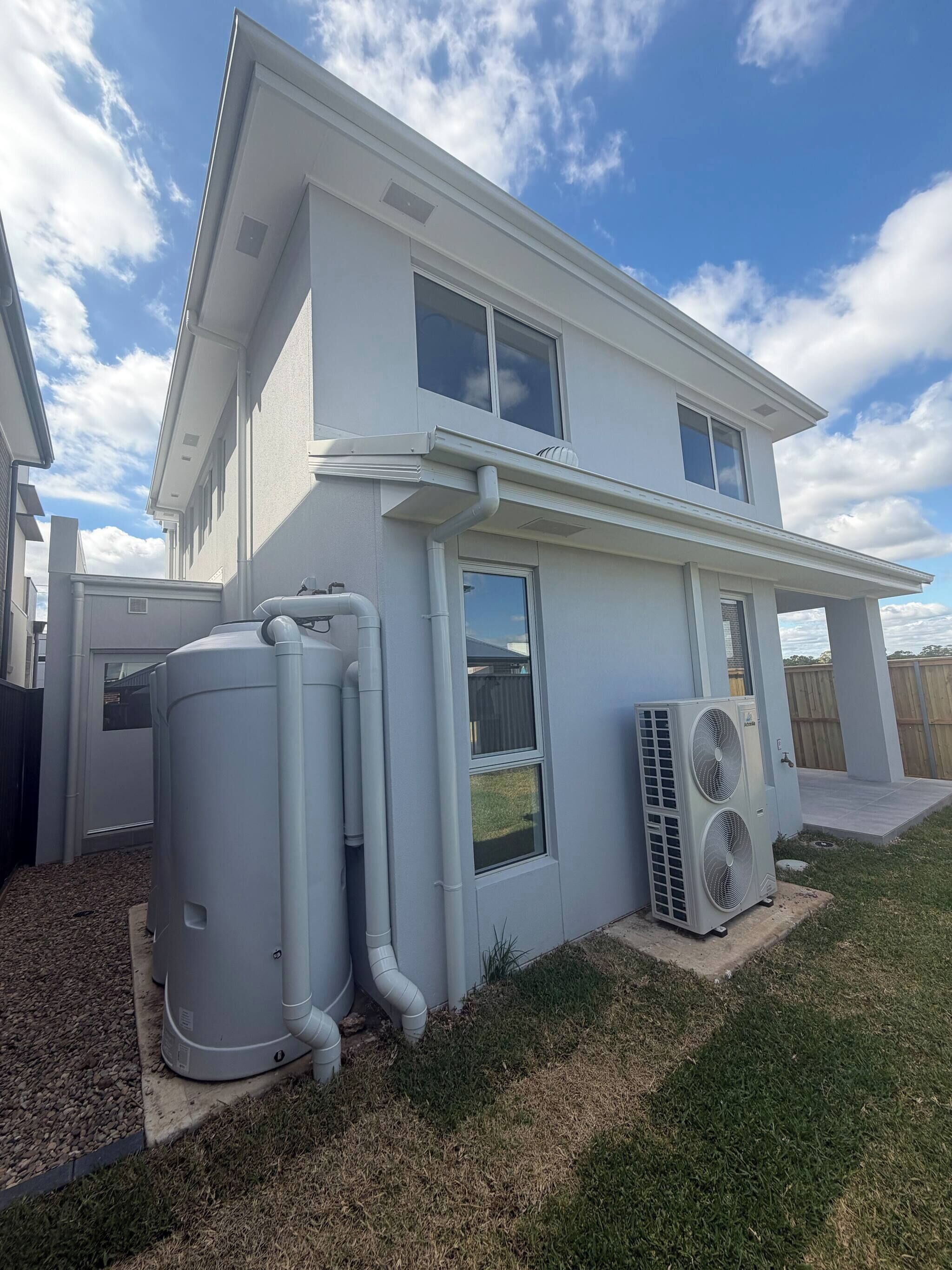 A two-story house with a white exterior, large windows, and an air conditioning unit.