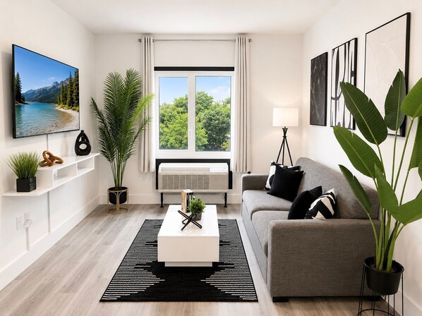 A modern living room with a flat-screen TV, a sofa, a coffee table, and large windows with curtains.