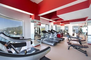 Ein Fitnessstudio mit Laufbändern, Trainingsgeräten und großen Fenstern mit Blick ins Freie.