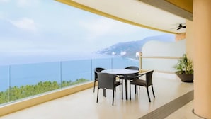 Un balcone con tavolo e sedie, una ventola a soffitto e vista sul mare.