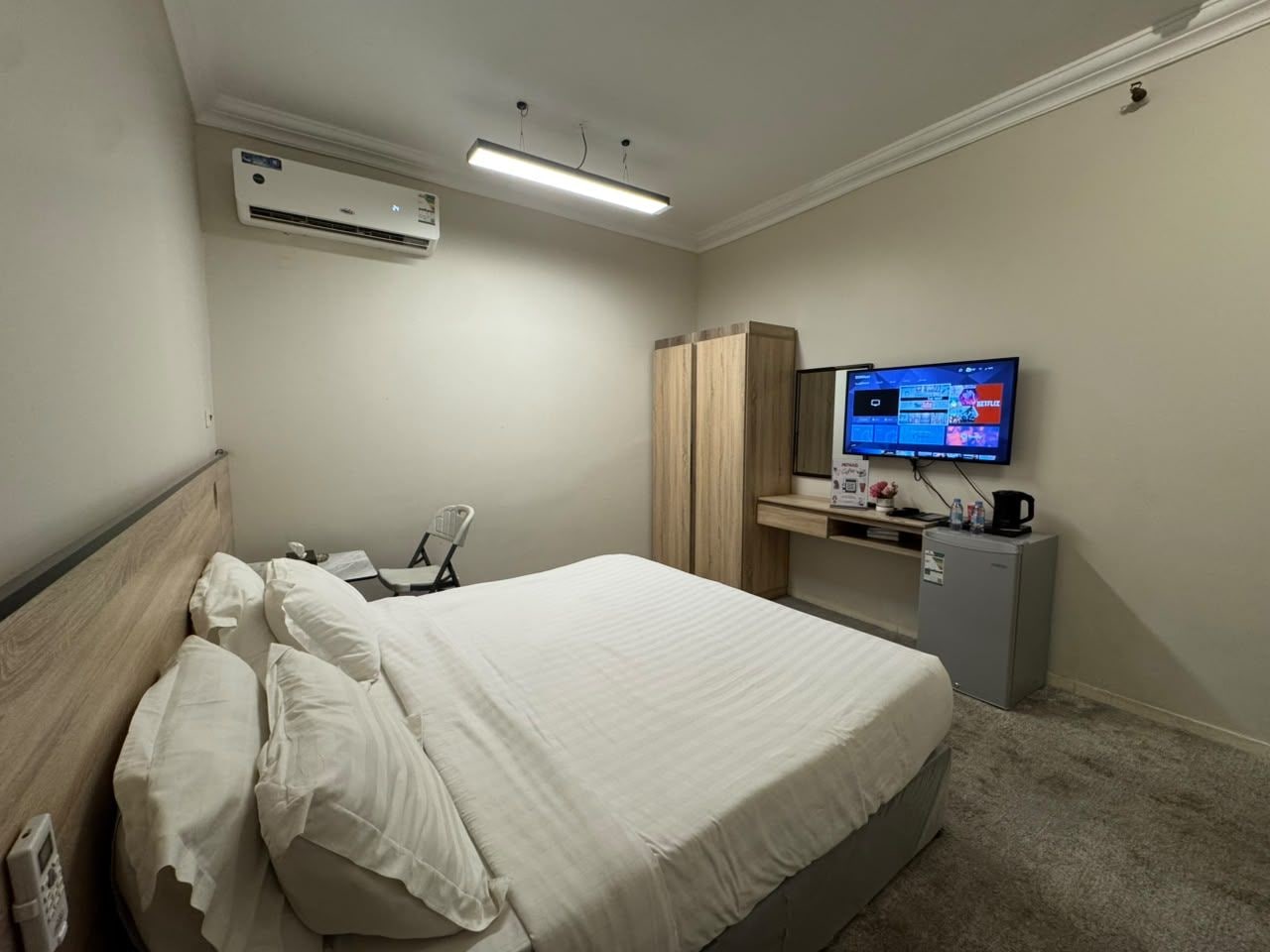 A hotel room with a bed, a desk, a television, and an air conditioning unit.