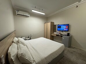 A hotel room with a bed, a desk, a television, and an air conditioning unit.