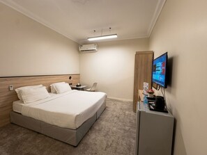 Habitación de hotel con cama, escritorio, silla, televisor y aire acondicionado.