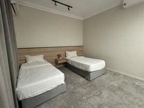 A hotel room with two single beds, a wooden headboard, a nightstand with a vase, and a carpeted floor. - Taq Al Masif Serviced Apartments (Tabuk)