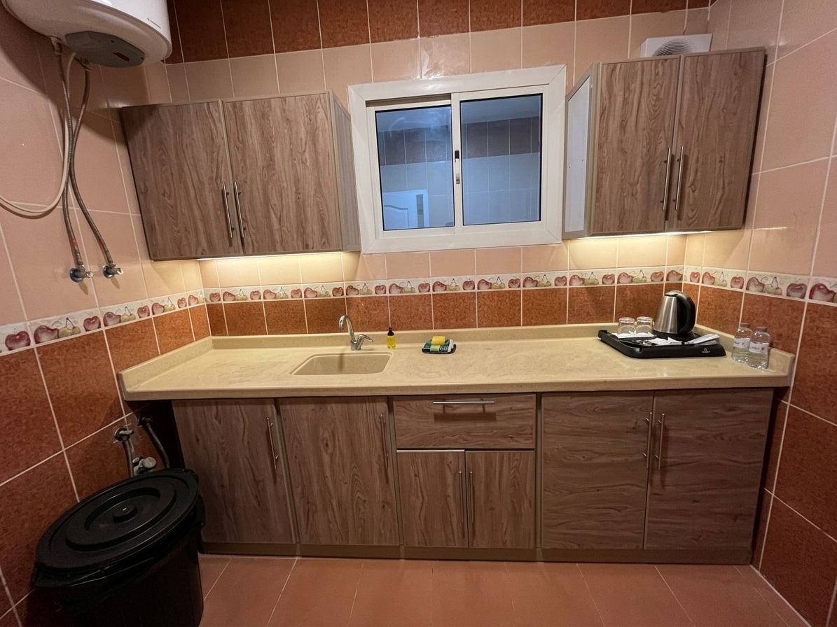 A kitchen with a sink, cabinets, a window, and a kettle on the counter.