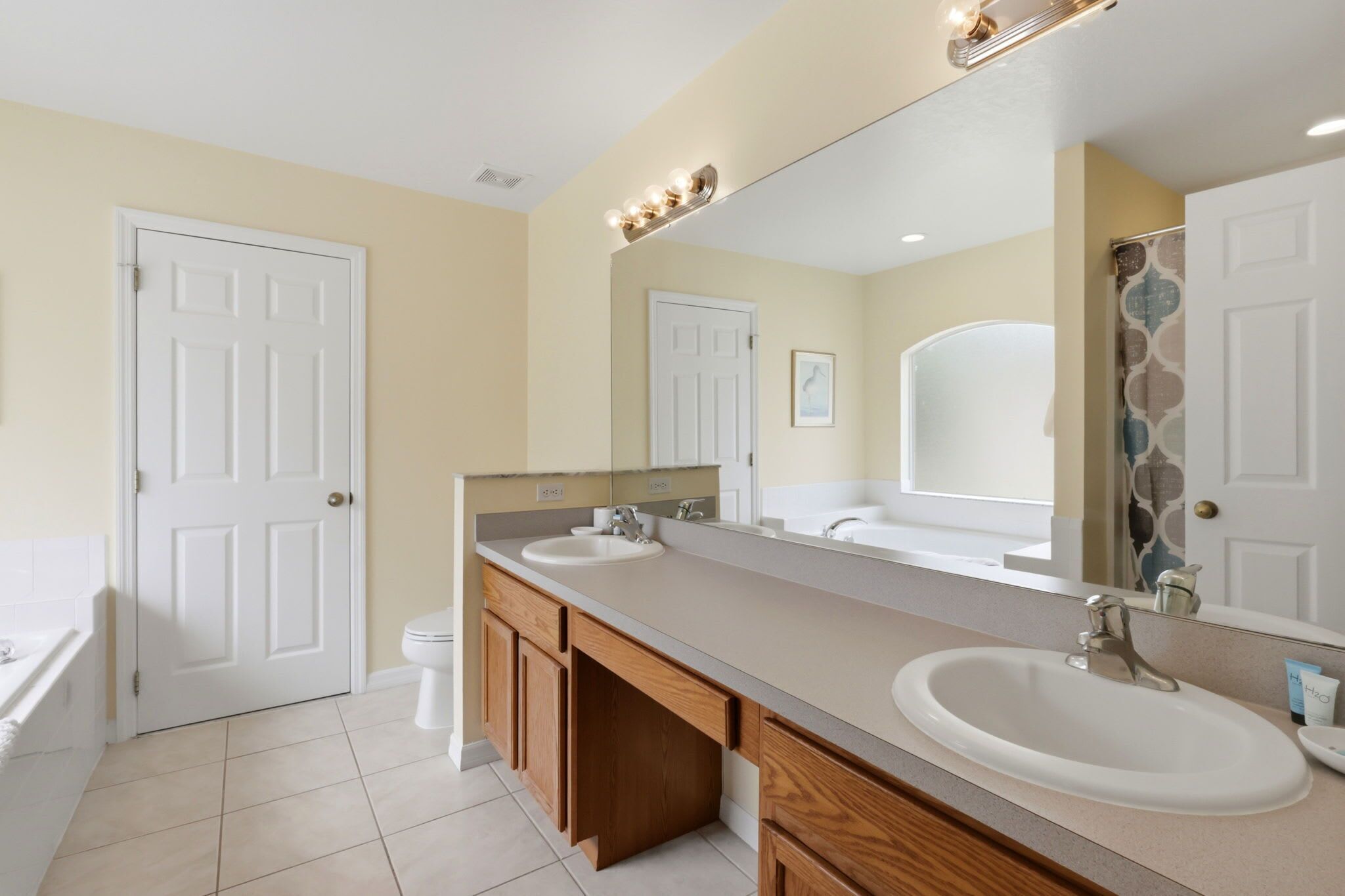A bathroom with two sinks, a bathtub, wooden cabinets, and a large mirror.