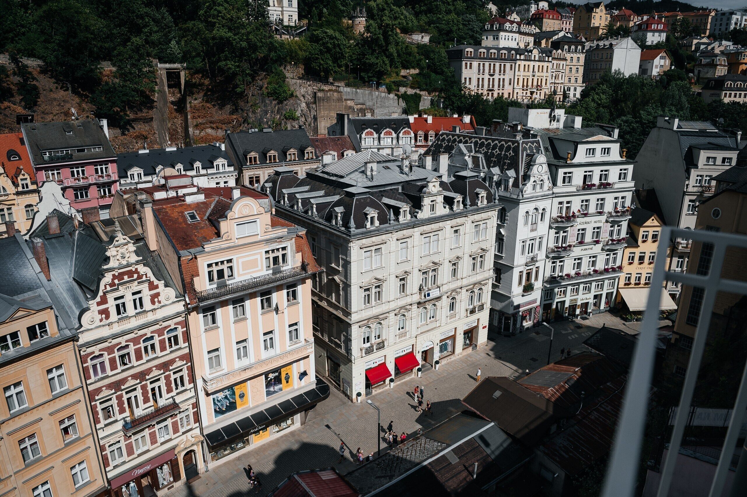Eine historische europäische Stadt mit traditioneller Architektur, darunter ein markantes Gebäude mit rotem Markisenvorhang und einem Schild für 'Lazensky Hotel'.