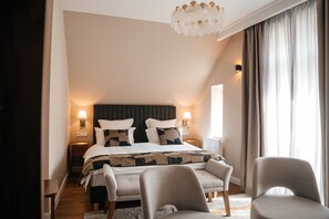 A hotel bedroom with a large bed, two bedside lamps, a chandelier, and a view of the outdoors. - Castle Hill Residence (Karlovy Vary)