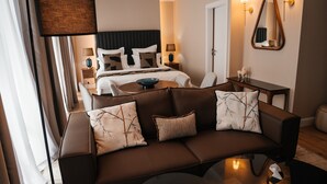 A modern hotel room with a brown leather sofa, a round coffee table, and a bed with a black headboard.