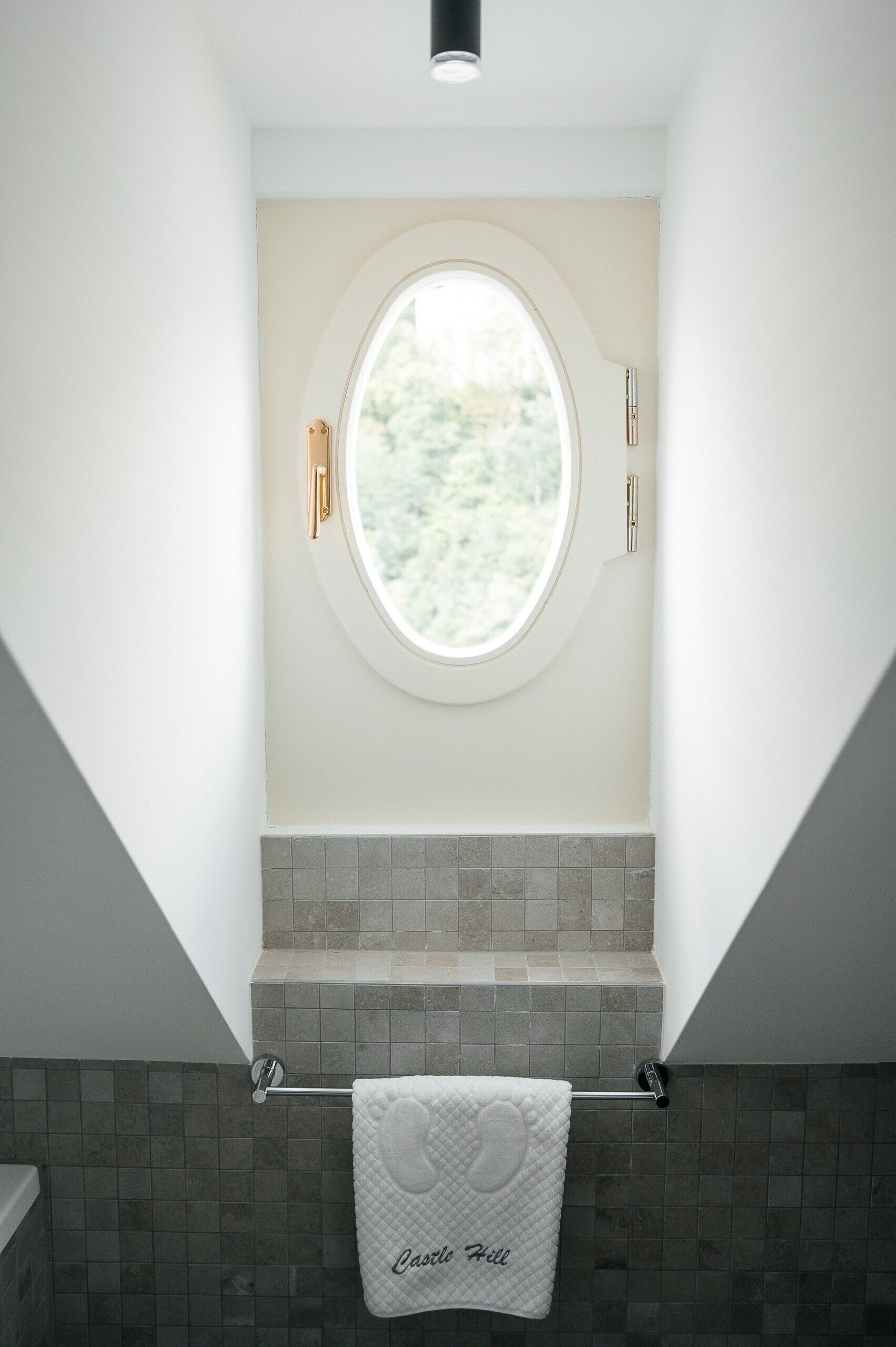 A bathroom with a bathtub, a towel rack with a towel, and a window with a view of greenery.