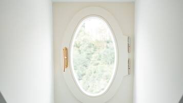 A bathroom with a bathtub, a towel rack with a towel, and a window with a view of greenery.