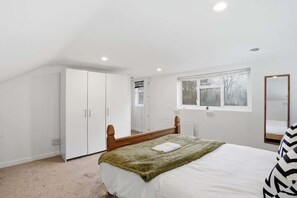 Ein Schlafzimmer mit Bett, Kleiderschrank, Fenster und Spiegel.
