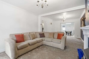 Ein Wohnzimmer mit einem beigefarbenen Ecksofa, einer Chandelier und einem Kamin, dekoriert mit einer Giraffefigur.