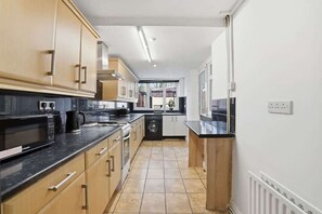 A kitchen with wooden cabinets, a black countertop, and a washing machine. - Coventry Stylish 4BR Home | Free Parking & Patio (Coventry)