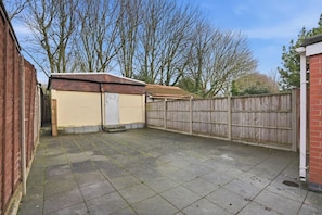 A backyard with a paved area, a wooden fence, and a brick wall. - Coventry Stylish 4BR Home | Free Parking & Patio (Coventry)