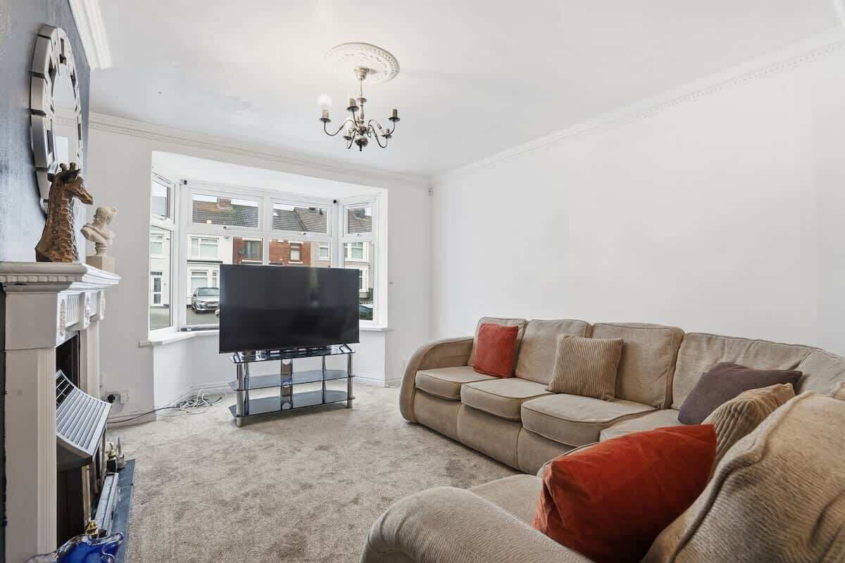 A living room with a television on a stand, a sofa with cushions, a fireplace, and a window with a view of buildings.