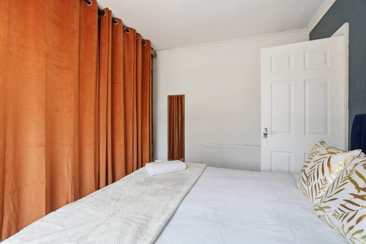 A bedroom with a bed, curtains, a radiator, and a door.