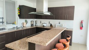 A modern kitchen with dark cabinets, a granite countertop, a built-in oven, a coffee maker, and a fire extinguisher.
