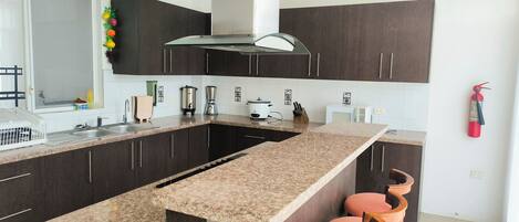 A modern kitchen with dark cabinets, a granite countertop, a built-in oven, a coffee maker, and a fire extinguisher.