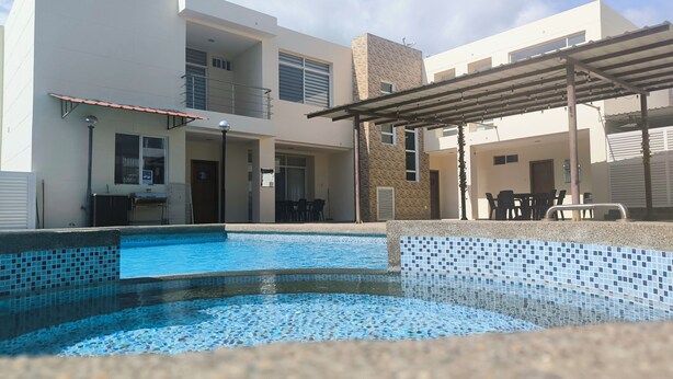 A swimming pool with tiled edges, a covered outdoor seating area, and a building with multiple windows and balconies.