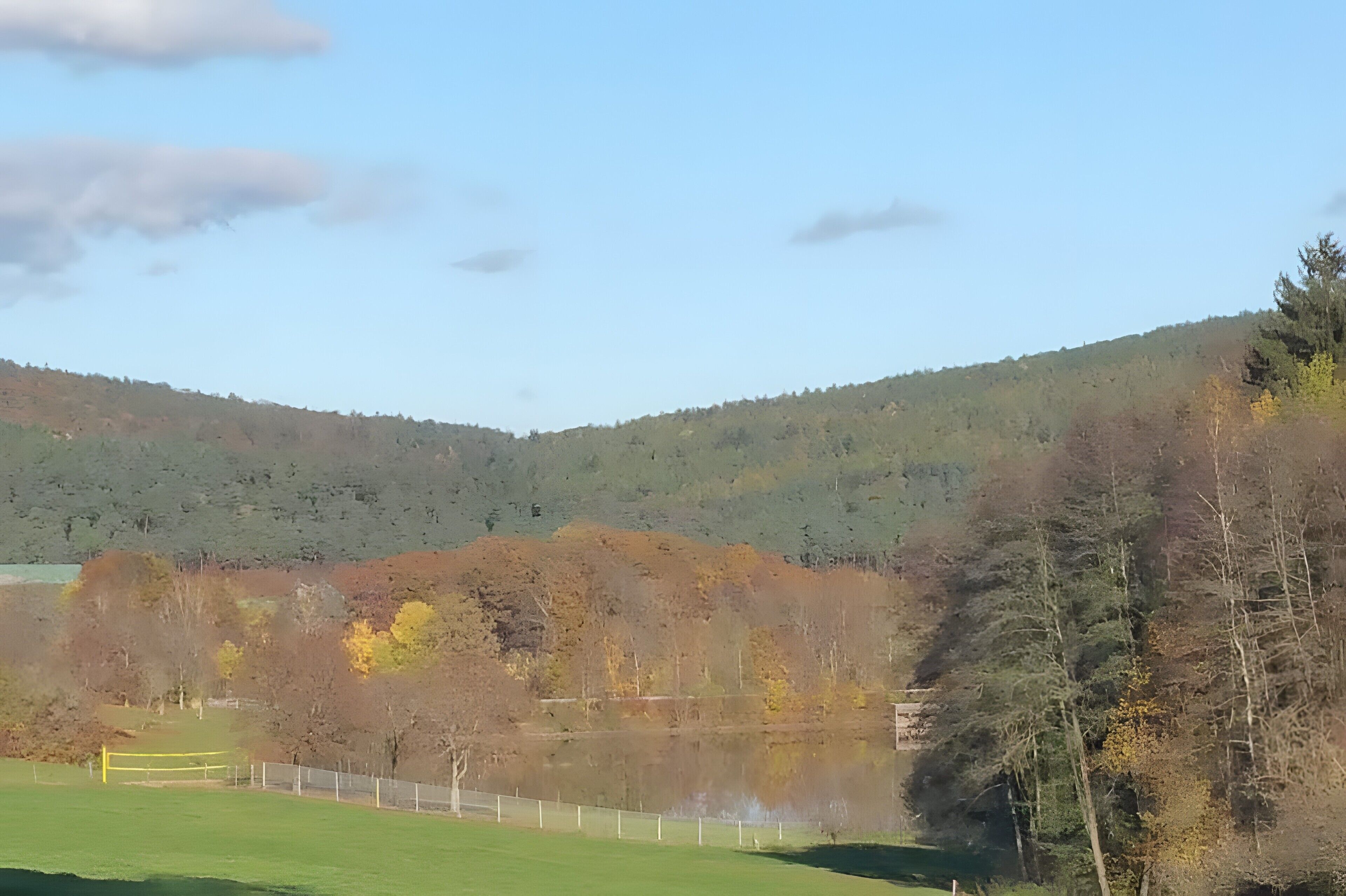 Un paysage comprenant un lac, des arbres et un arrière-plan vallonné.