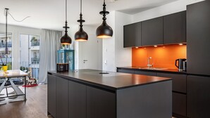 A modern kitchen with dark cabinetry, a central island, pendant lighting, and a view of the outdoors. - Modern, Spacious Apartment in a Residential Neighborhood (Freiburg im Breisgau)