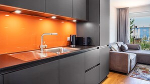 A modern kitchen with a built-in sink, a coffee machine, and a dining area with a sofa and a view of the outside. - Modern, Spacious Apartment in a Residential Neighborhood (Freiburg im Breisgau)