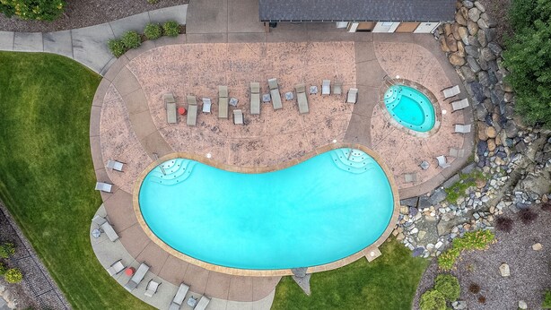 A large irregularly shaped swimming pool with a hot tub, surrounded by lounge chairs and a stone wall. - Golf Course Townhome 3 bed/3 bath, Private Hot Tub (Columbia Falls)