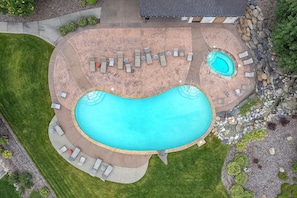 A large irregularly shaped swimming pool with a hot tub, surrounded by lounge chairs and a stone wall. - Golf Course Townhome 3 bed/3 bath, Private Hot Tub (Columbia Falls)
