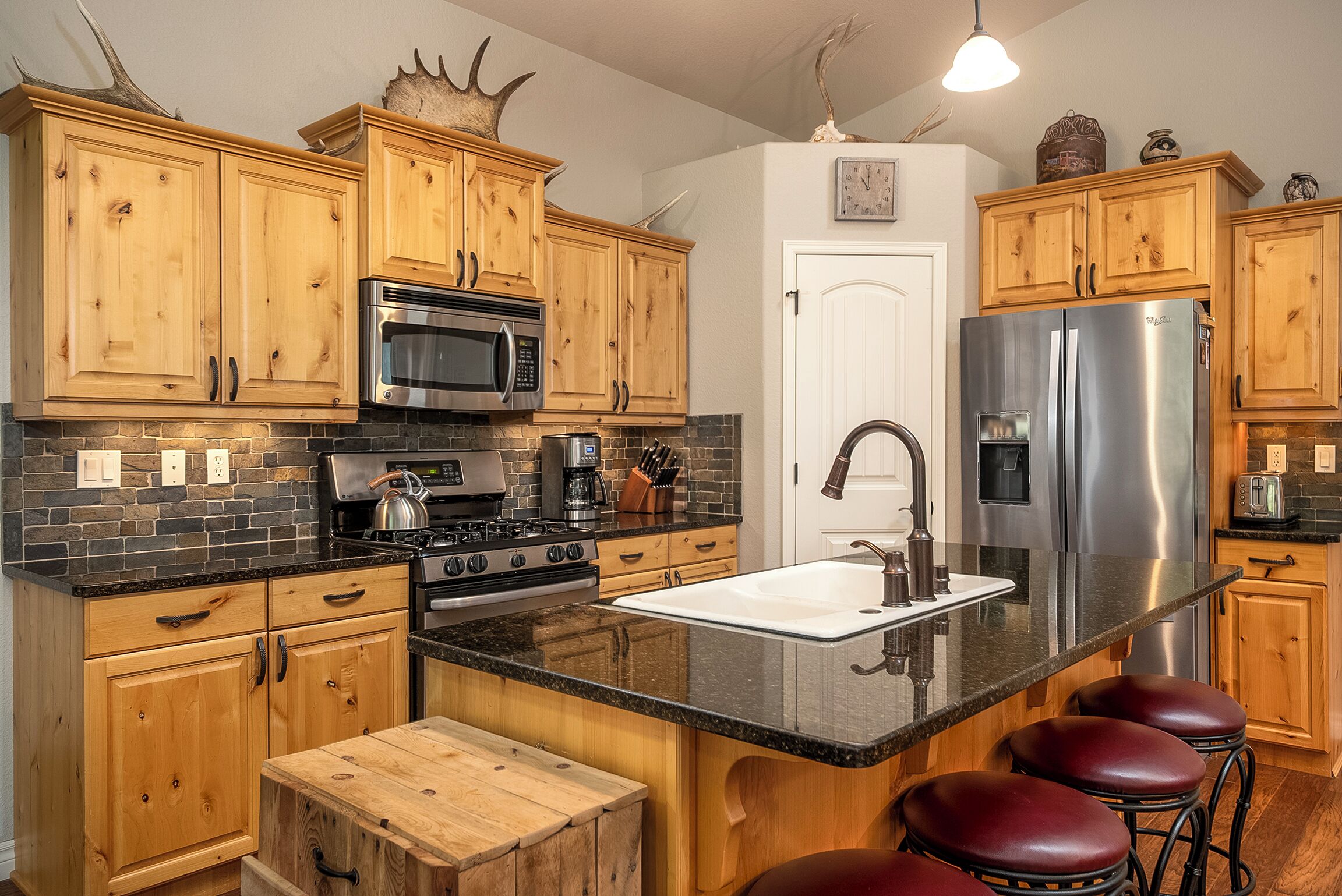 A kitchen with wooden cabinets, a stainless steel refrigerator, a built-in oven, and a large island with stools.