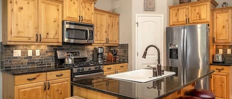 Une cuisine avec des meubles en bois, un réfrigérateur en acier inoxydable, un four encastré et un grand îlot central doté de tabourets.