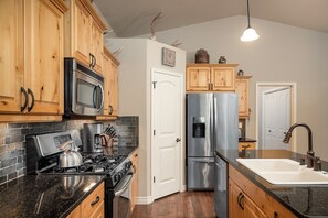 Una cocina con gabinetes de madera, electrodomésticos de acero inoxidable, una encimera negra y una puerta blanca.