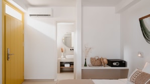 A bedroom with a bed, a bedside table, a wardrobe, a bathroom with a mirror, and an air conditioning unit.