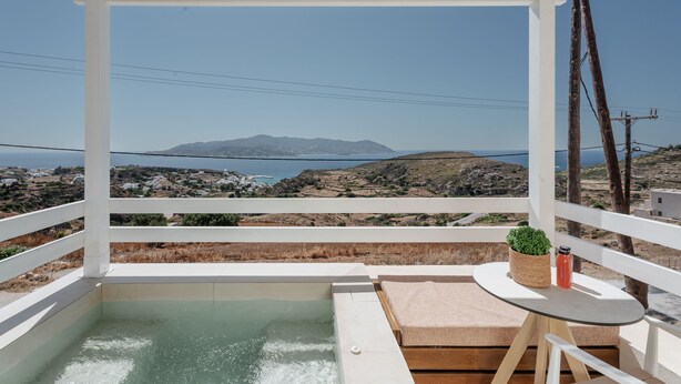 A balcony with a view of the sea, a hot tub, a table with a plant, and a wicker basket.