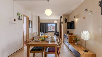 A dining area with a wooden table and chairs, a TV mounted on the wall, and a window with curtains.