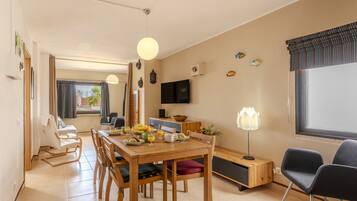 A modern living room with a dining table, chairs, a TV, and a sofa.