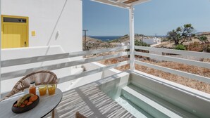 A balcony with a table, chairs, and a view of the sea and landscape.