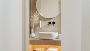 A bathroom with a white sink, a mirror, a vase with dried plants, and towels on a shelf.
