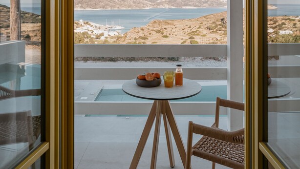 Ein modernes Zimmer mit Glaswand, einem runden Tisch und einem Stuhl, mit Blick auf Meer und Hügel.