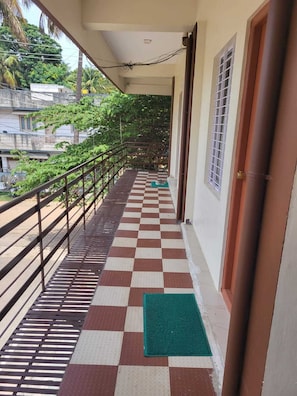 A corridor with a checkered floor, a green mat, a metal railing, and a door. - Sri Durga Homestay (Mysore)