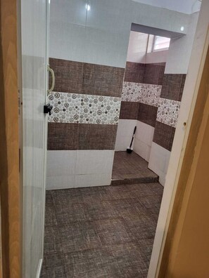 A bathroom with a tiled floor, a shower area, and a toilet. - Sri Durga Homestay  (Mysore)