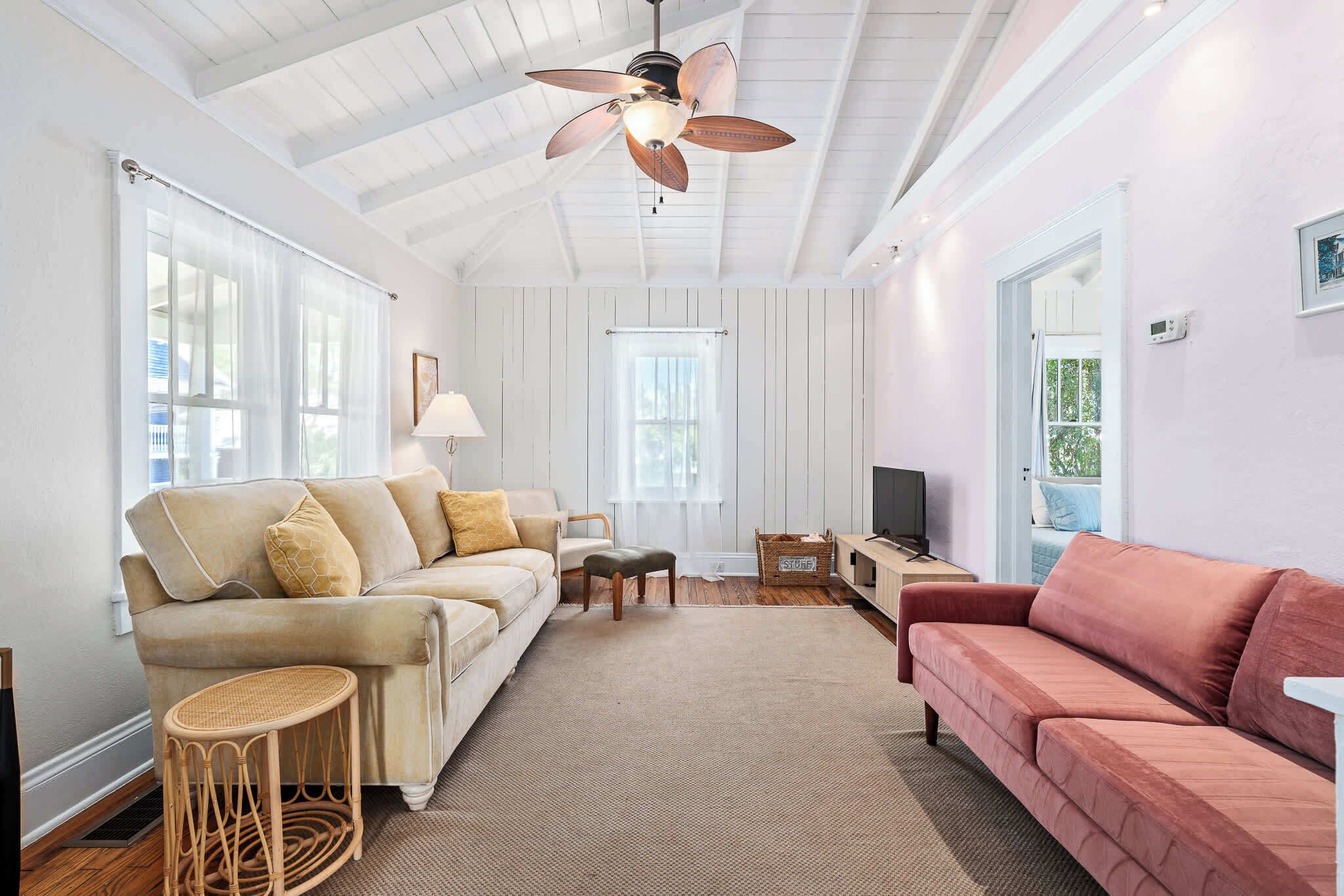 A living room with a beige sofa, a pink sofa, a ceiling fan, and a television.