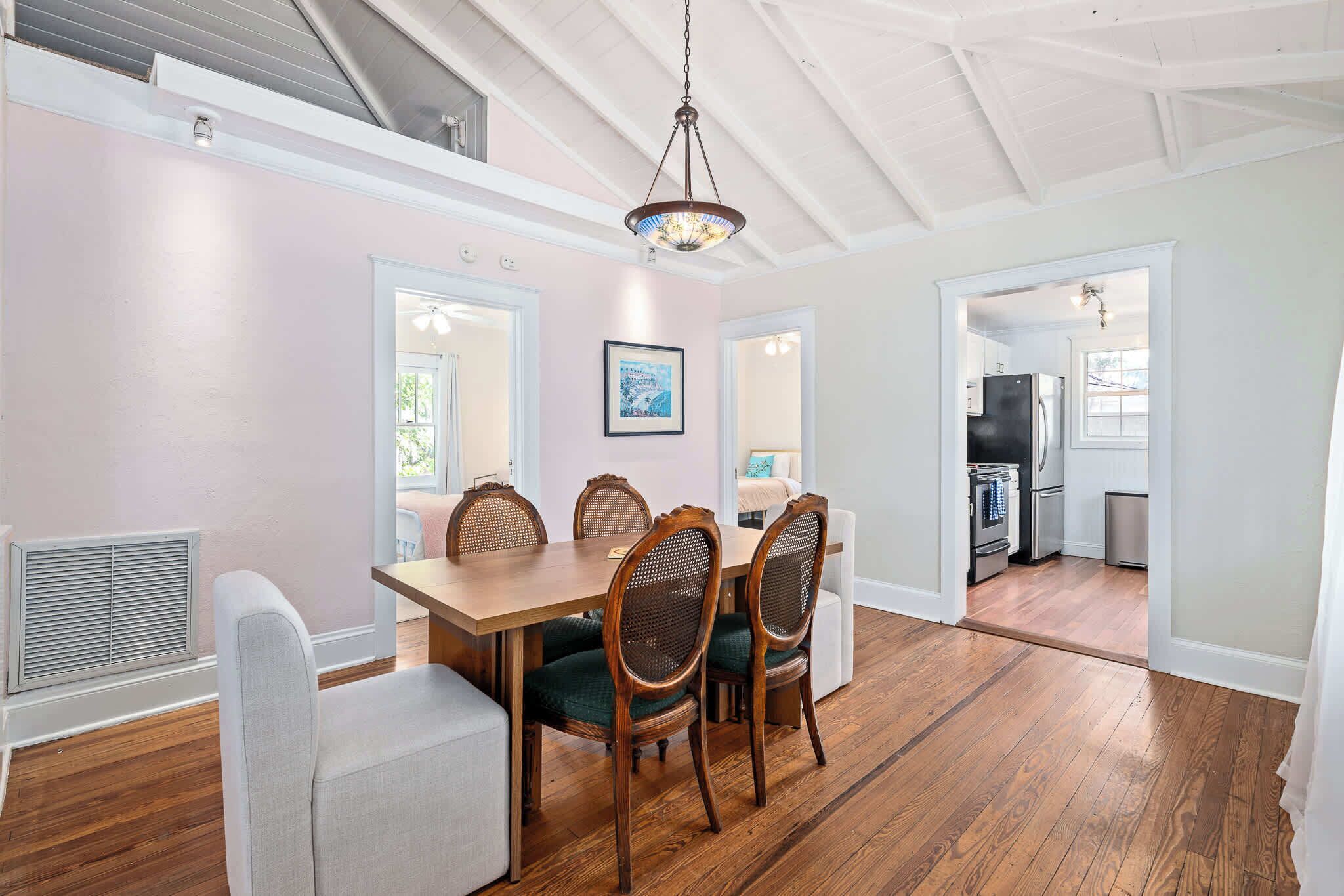 A dining area with a wooden table and chairs, a ceiling fan, and a view into the kitchen.