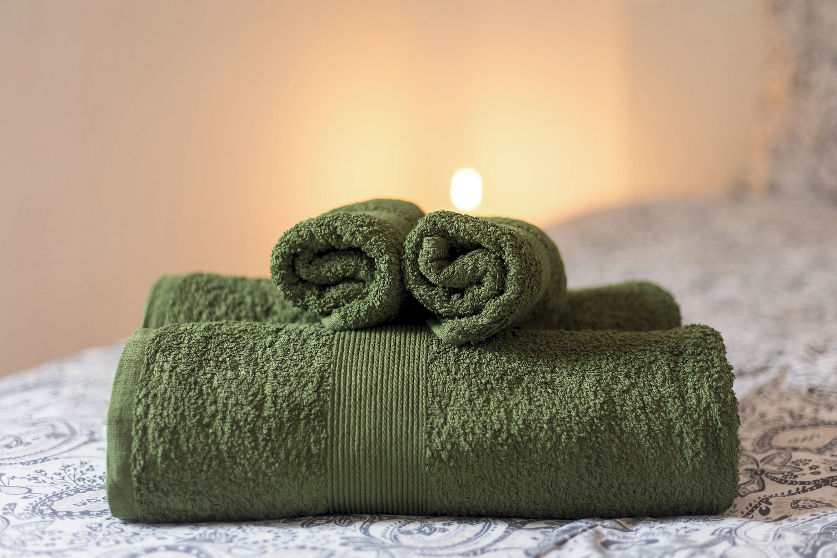 A bed with rolled green towels and a lit candle in the background.